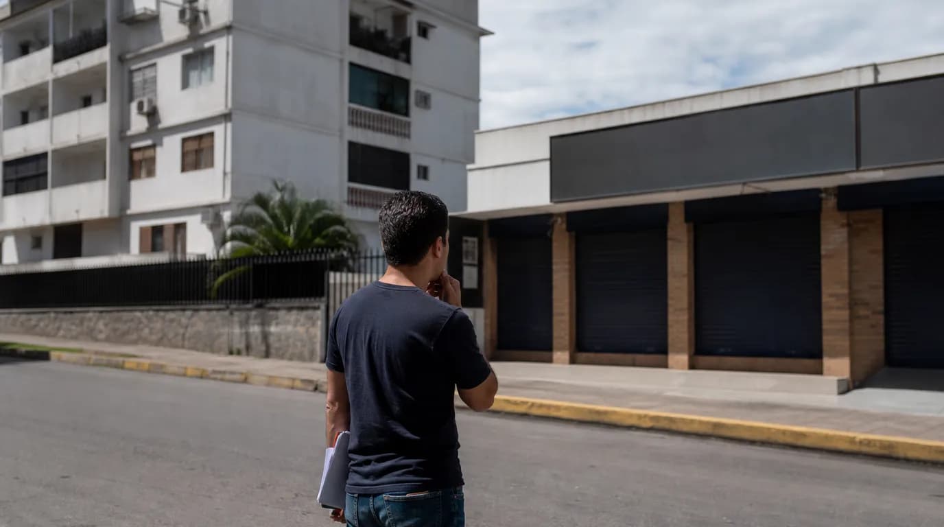 Thoughtful investor comparing two real estate investment options, a residential building and a row of commercial spaces, in a Venezuelan urban area