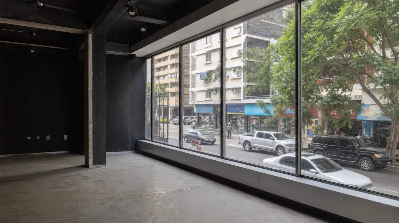 Empty commercial space with a wide storefront window on a busy avenue in a Venezuelan city, overlooking buildings and shops