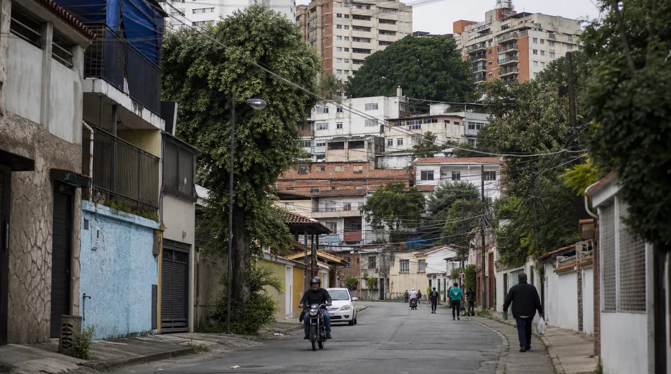 Mixed-density Venezuelan residential street with apartment blocks, houses, power lines, and neighborhood shops