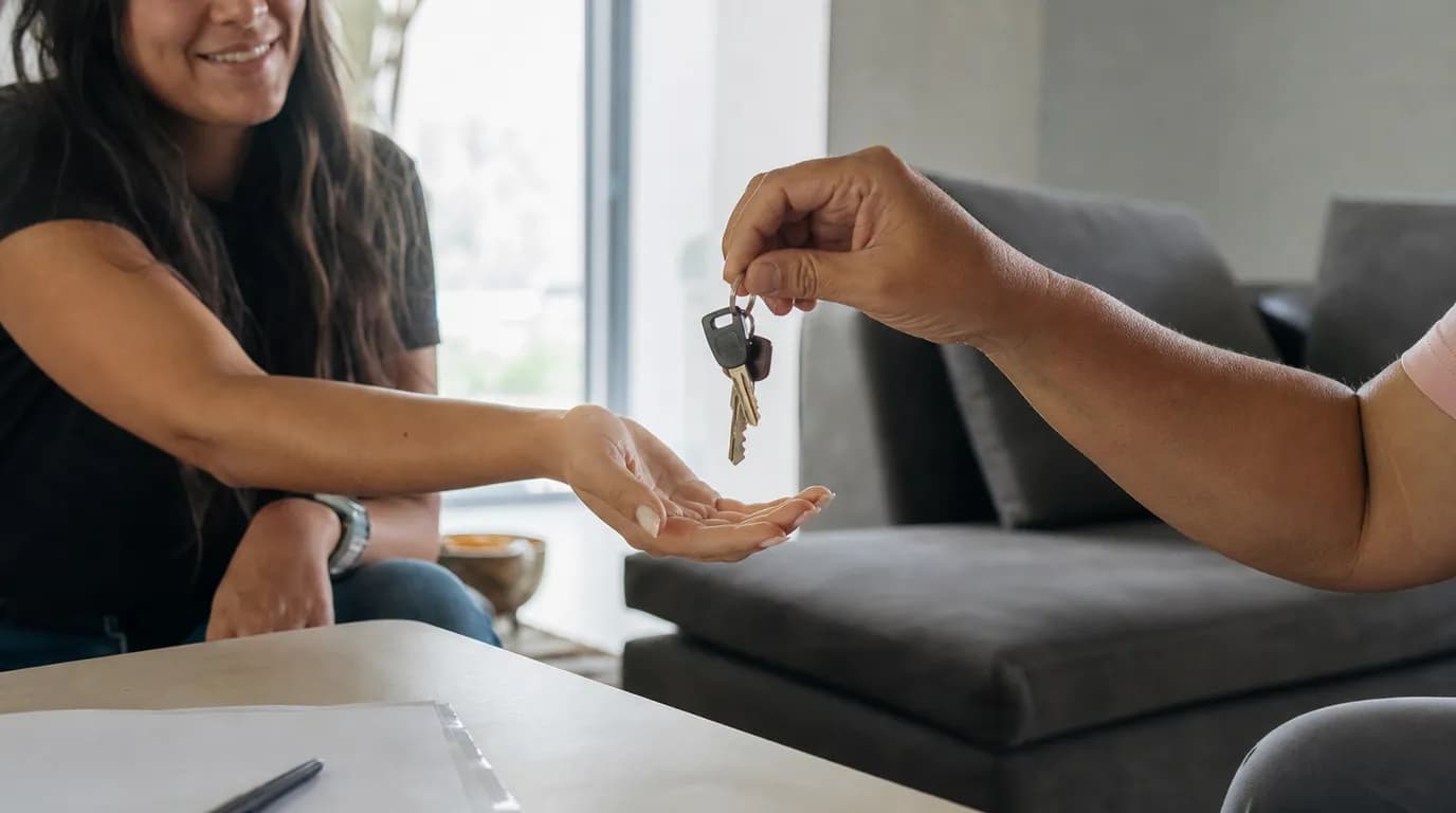 Llaves de una vivienda pasando de una mano a otra sobre la mesa de una sala moderna y luminosa